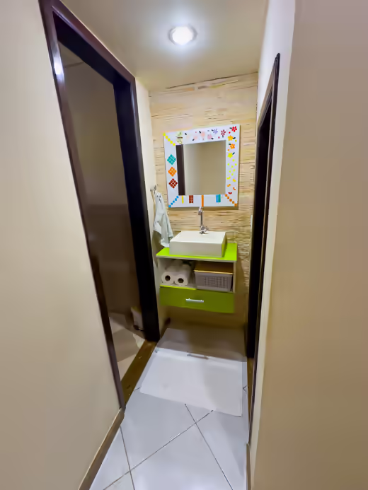 Lavabo junto à sala, com bancada verde e espelho